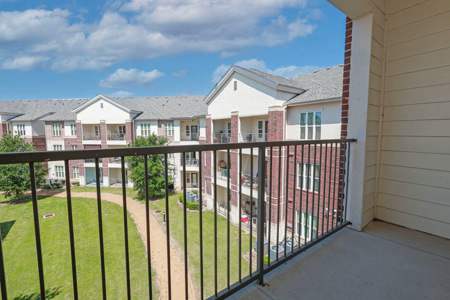 A balcony overlooks a grassy area and apartment buildings.