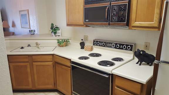 A kitchen with a black cat sitting on the stove.