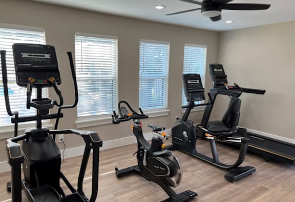 Three exercise bikes are lined up in a room with a ceiling fan.