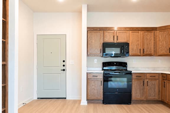 A kitchen with a black fridge and microwave, wooden cabinets, and a white door.