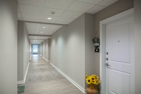 A long hallway with a door on the right and a vase of flowers on the floor.