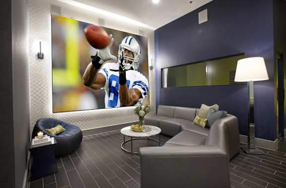 A football player in a blue and white uniform is catching a football in a modern living room.