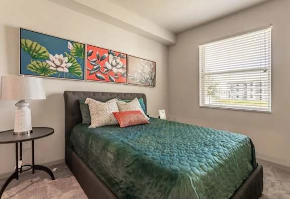 A bedroom with a bed, a table, and a painting on the wall.