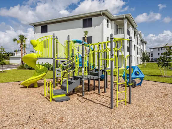 A playground with a yellow slide and a white building in the background.
