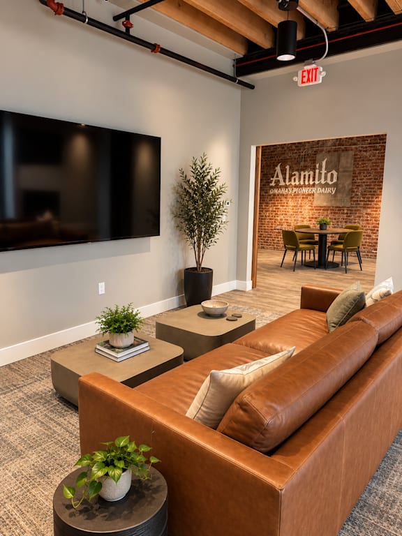 A brown leather couch in a room with a flat screen TV mounted on the wall.