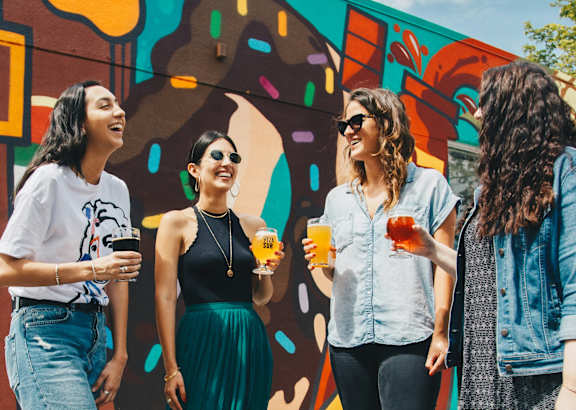 Four women are standing in front of a colorful wall.