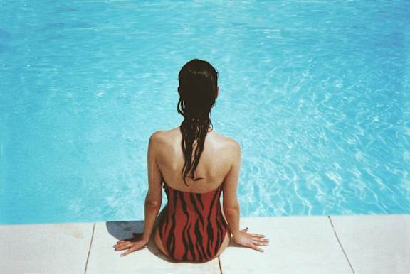 A woman in a striped swimsuit sits by a pool.