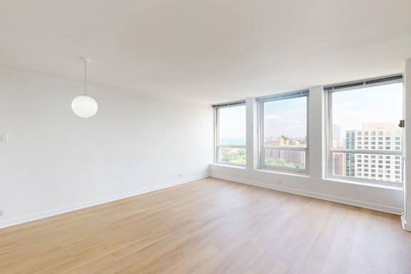 A room with wooden floors and three windows overlooking a cityscape.
