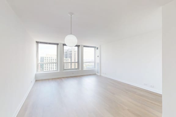 A room with a white ceiling, wooden floor, and a large window with a view of a cityscape.