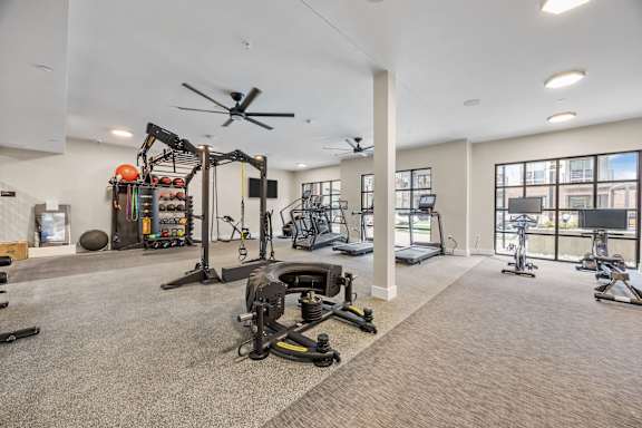 A spacious gym with a variety of equipment including a weight bench, a treadmill, and a ceiling fan.at Adler Montford Park + Drexel Townes, North Carolina, 28209