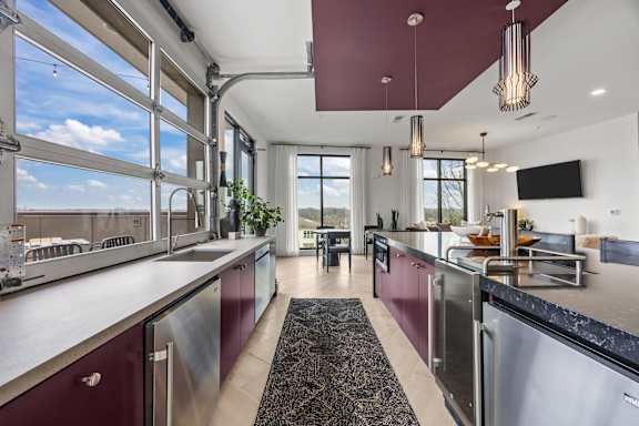 A modern kitchen with stainless steel appliances and a maroon accent wall.at Adler Montford Park + Drexel Townes, North Carolina, 28209