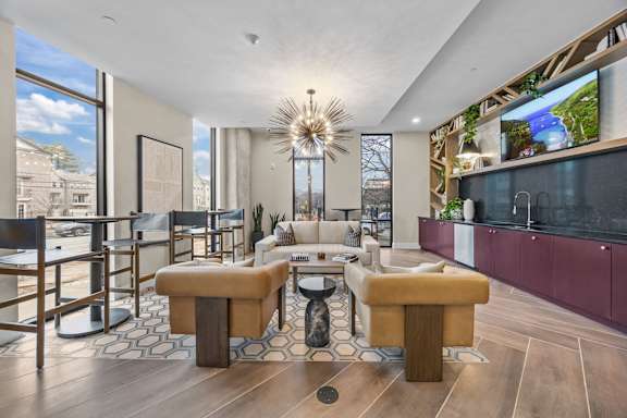 A modern living room with a large window, a sofa set, and a kitchen area.at Adler Montford Park + Drexel Townes, North Carolina, 28209