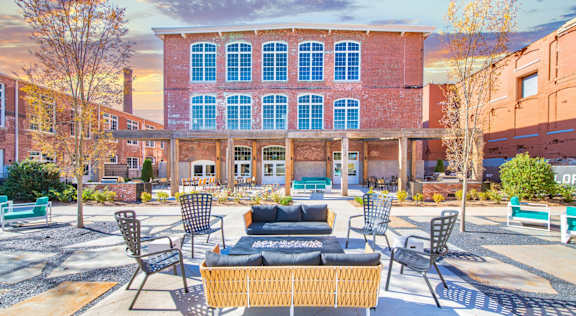 A courtyard with a wicker sofa and chairs in front of a red brick building at Judson Mill Lofts, South Carolina 29611