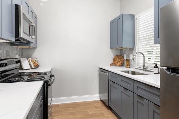 a kitchen with gray cabinets and white countertops and a stainless steel stove and sink