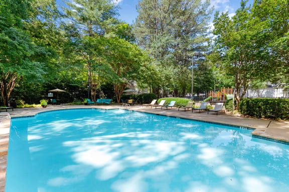 a swimming pool with trees and chairs around it