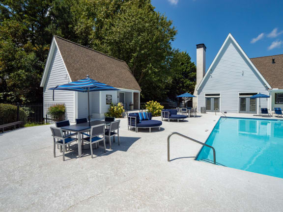 a swimming pool with a table and chairs next to a house with a chimney