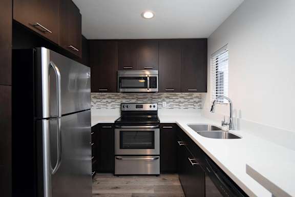 A modern kitchen with dark wood cabinets and stainless steel appliances.