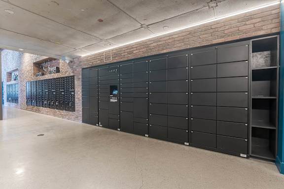 Mail room with parcel lockers and brick accent wall at AMP 30 Apartments, San Diego, California