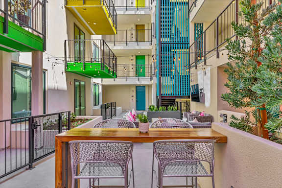 A patio with a table and chairs overlooks a courtyard with a fence and a tree.