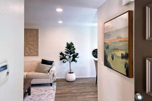 A living room with a couch, a potted plant, and a painting on the wall.