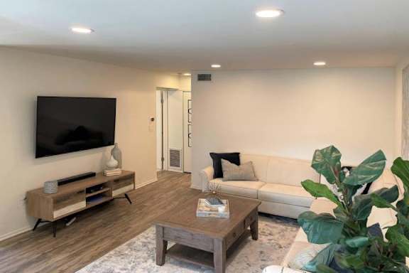 A modern living room with a white couch, a wooden coffee table, and a flat-screen TV mounted on the wall.
