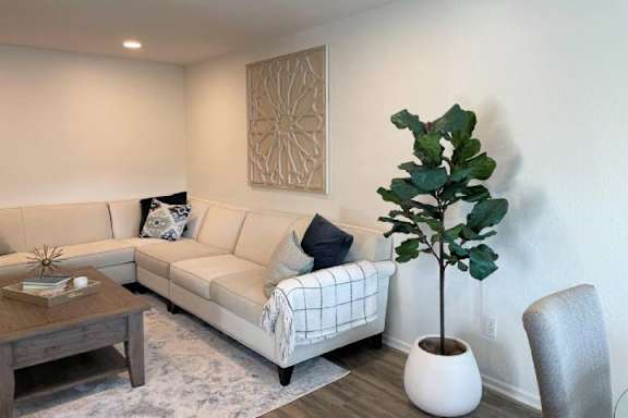 A living room with a couch, a coffee table, a plant, and a wall art.