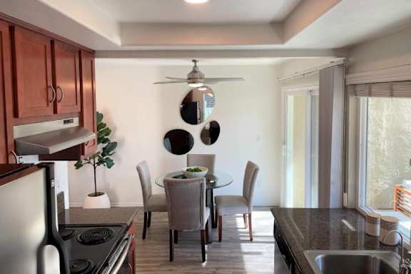 A kitchen with a stove top oven, a sink, a dining table with chairs, and a ceiling fan.