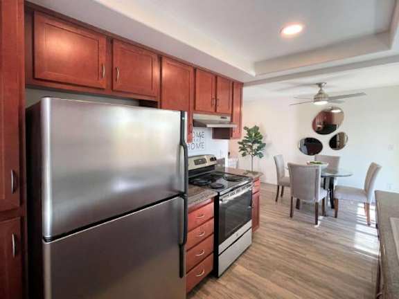 A kitchen with a stainless steel refrigerator, wooden cabinets, and a dining area with a table and chairs.
