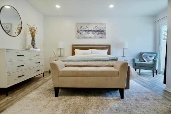 A bedroom with a beige bed, a white dresser, and a grey armchair.