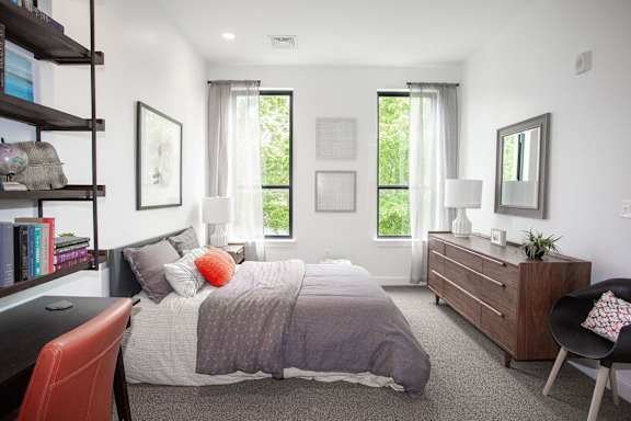 A bedroom with a bed, nightstand, chair, and window.