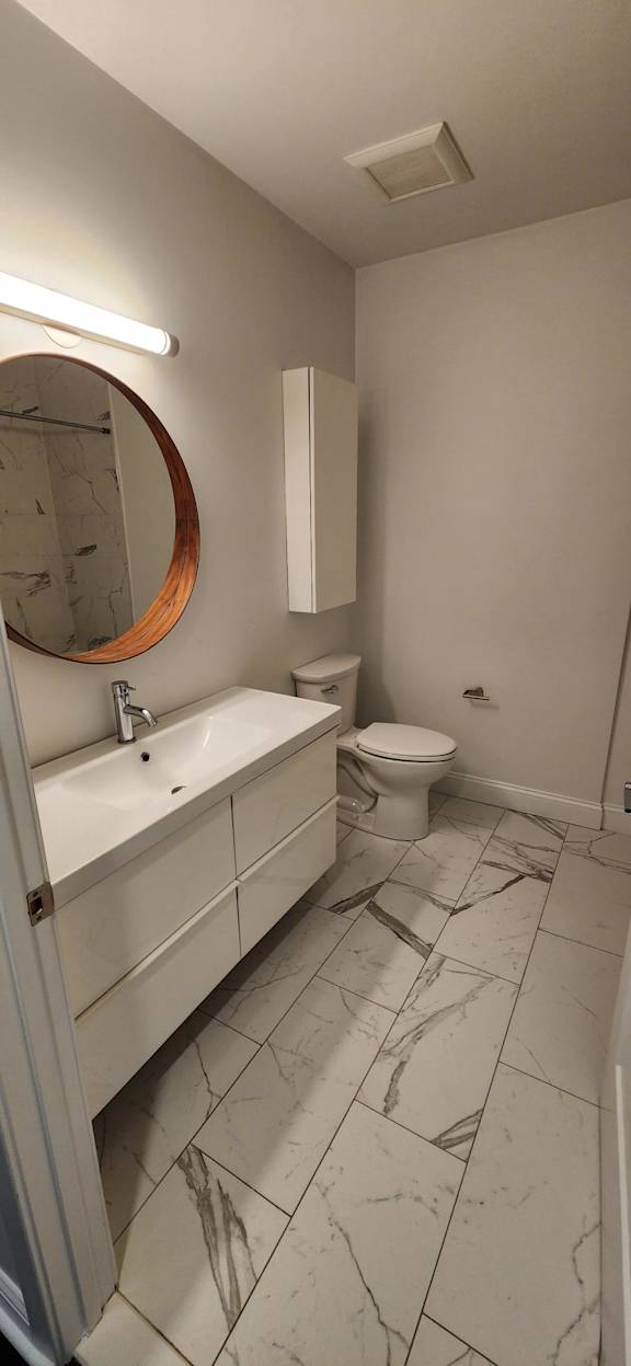 A bathroom with a toilet, sink, and mirror.