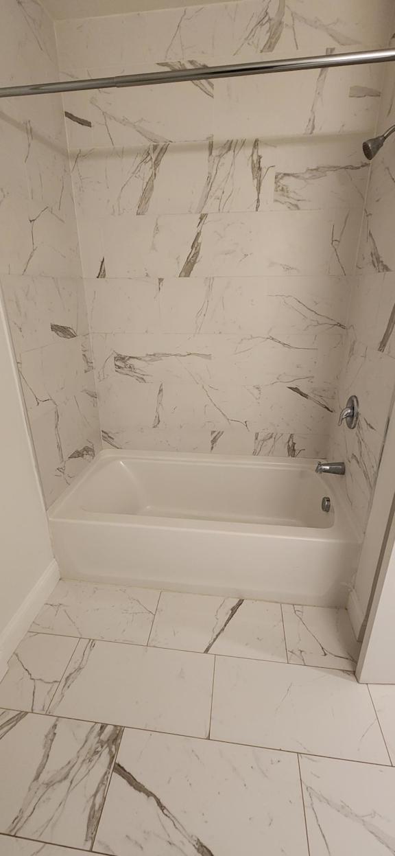 A white marble tiled shower with a white tub.
