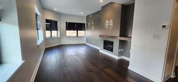 A large, empty living room with wood floors and a fireplace.