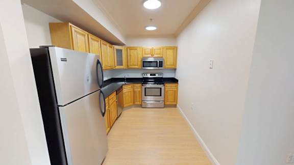Galley kitchen with light wood cabinetry and black countertops at Bostonian Shoe Lofts Apartments, Whitman