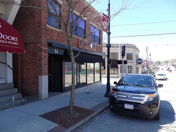 A black SUV is parked on the sidewalk in front of a yoga studio.