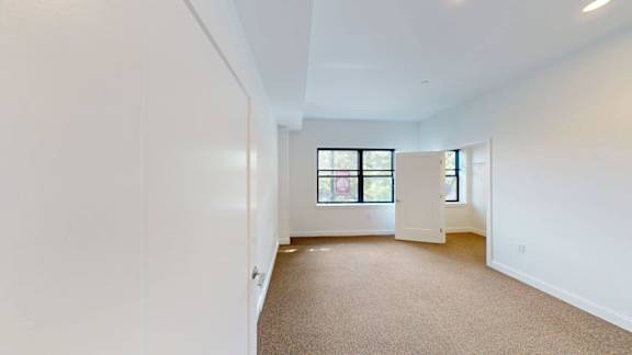 Empty studio apartment with carpet and windows at Ten Front Apartments, Weymouth, MA