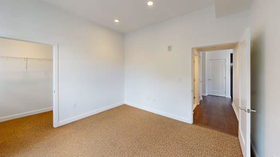 Bedroom with beige carpet and closet entrance at Ten Front Apartments, Weymouth, MA