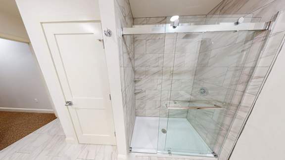 A bathroom with a walk-in shower and a white door.