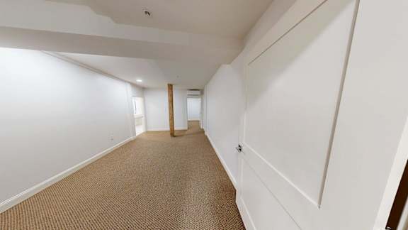 A long hallway with white walls and carpeted floor.