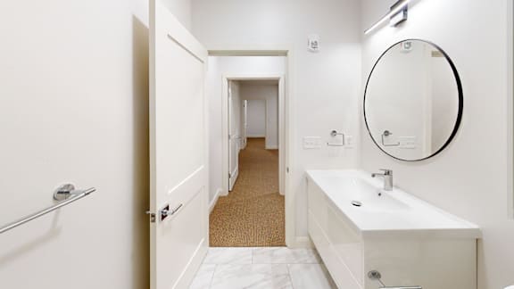 A white bathroom with a round mirror and a white sink.