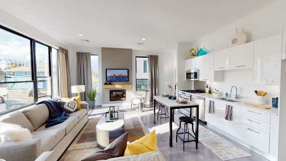 A modern living room with a grey sofa and a white kitchen.