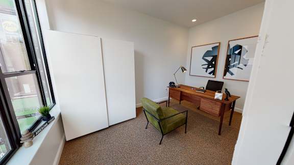 A room with a desk, chair, and two pictures on the wall.