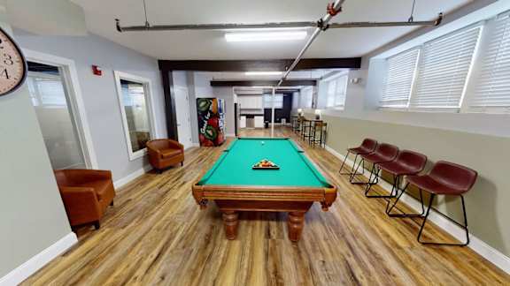 A pool table in a room with wooden flooring and chairs.
