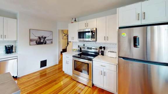 A kitchen with white cabinets and a wooden floor.