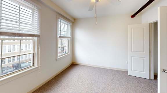 Bright bedroom with two windows and carpet flooring at Bostonian Shoe Lofts Apartments, Whitman, MA 02382
