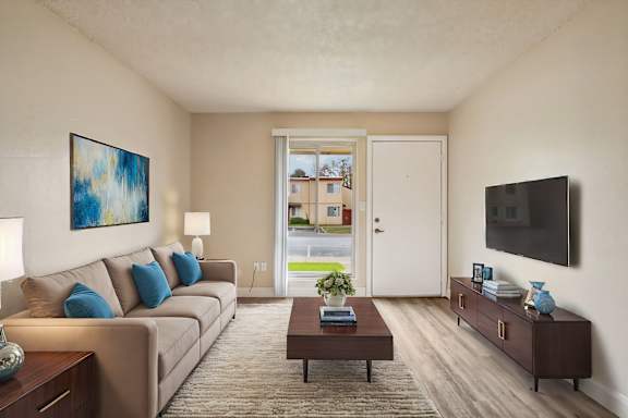 A living room with a brown couch, a coffee table, a painting, a lamp, a flat screen TV, and a door leading to a balcony.