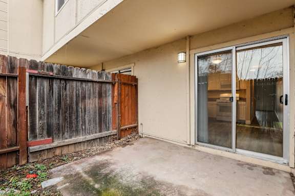 A patio with a sliding glass door and a wooden fence.