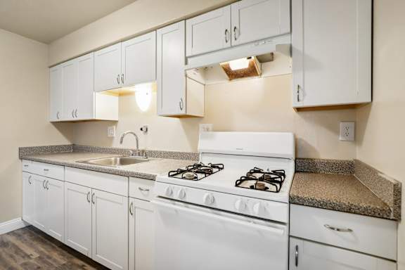 A white kitchen with a stove, sink, and cabinets.