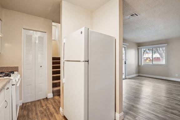 A white refrigerator in a kitchen with wood floors and a staircase.