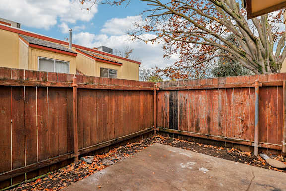 A brown wooden fence with leaves on the ground.